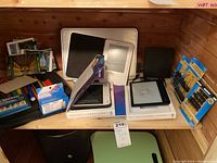 Shelf view with two Kobo eReaders, an Amazon Kindle, postcards, pens, binder clips, waste basket and a green foldable laptop table