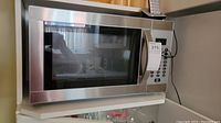 Full view of Danby microwave oven showing stainless steel body, control panel with keypad and handle, placed on a white shelf.