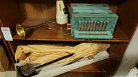 Shelf containing brass horn, white horn-like instrument, blue steel reeds accordion, and wrapped stringed instrument.