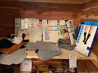 Lot of men's microfiber dress socks, medical compression socks, and women's pantyhose displayed on wooden surface, most in original packaging.