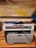 Brother DCP-7040 multifunction printer front view with control panel and brand logo visible. Power cord also visible.