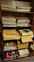 Wooden shelving filled with stacks of vinyl records and several cardboard boxes containing more records.