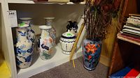 Photo showing five Asian-style vases on a shelf, various designs predominantly blue and white with one purple vase with orange flowers containing peacock feathers