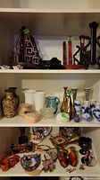 Wide view of multiple shelves showing diverse vases, figurines, souvenir items including Asian style ceramics and novelties