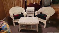Wicker furniture set including two arm chairs with cushions, a coffee table and lift-top storage side table arranged in a room.