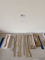 Table display of twelve chain necklaces laid side by side across three trays and on tabletop