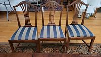 Three side chairs with carved wooden backs and blue-beige striped seats, showing front view.