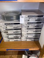 Stacked boxes of glass dinner plates and visible loose plates on shelf.