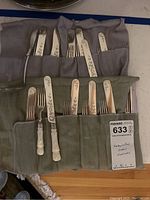 Full view of the flatware set stored in fabric rolls showing knives and forks with mother of pearl handles and engraved blades and tines.