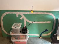 Green wooden layout board leaning against wall with three stacked clear plastic tubs