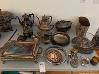 View of entire lot showing multiple silver-plated items arranged on table including coffee and teapots, trays, candleholders, and cooler.