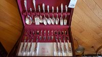 Full view of Holmes and Edwards silver plate flatware set arranged in original wood box with red velvet lining including forks, spoons, knives and spreaders.
