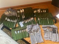 Multiple felt cloth rolls displaying rows of forks, knives, spoons and spreaders on wood floor