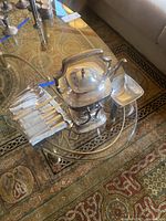 Overview of sterling teapot on stand with utensils roll and silver bowl on glass table