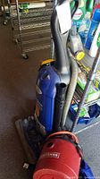 View of blue Eureka upright vacuum beside a red Craftsman shop vacuum on the floor.