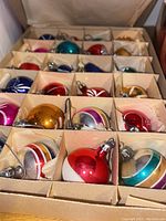 Close-up of vintage glass ball Christmas ornaments in original cardboard box with compartments showing multiple colors and white painted designs.
