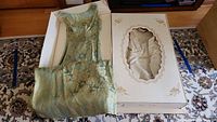 Florencia vintage wedding dress in pale green-blue floral lace laid out next to decorated box