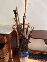 Photo showing the collection of nine walking sticks and canes along with two umbrellas arranged inside a ceramic vase against a white wall.