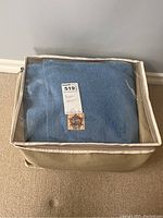 Beige fabric storage case with clear plastic top showing folded blue wool blanket inside.