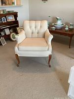 Front view of the vintage tufted back armchair with light upholstery and wooden legs.