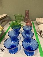 Overview of blue dessert cups, pink vase, pink decanter with glass, green juicer and measuring cup on table