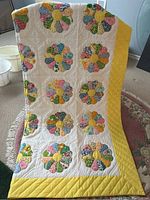 Full view of handmade Dresden Plate quilt showing multiple colorful fabric petals and yellow center, with a yellow border and white background.