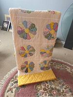 Full view of quilt folded and displayed showing the Dresden Plate pattern with multicolored floral petals and yellow centers on a cream background with yellow border.