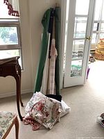 Partial rolls of various fabric types, mostly upholstery and drapery fabric including floral print and solid colors leaning against a windowed door.
