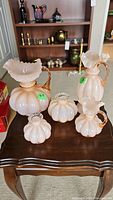 Five pink Fenton style glass vases with ruffled edges and pumpkin shapes on wooden table.