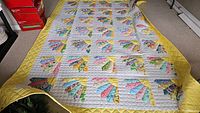 Full view of handmade twin size quilt laid flat, showing patchwork fan blocks in multiple colors on white background with yellow border.