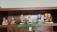 Photo showing 6 Goebel Hummel figurines lined up on a shelf, including various children in classic poses.