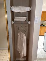 View of folded napkins on top and folded tablecloth below hanging in small closet area