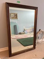 Full view of the rectangular mirror leaning against a wall, showing the brown bamboo-style wooden frame and clear reflective surface.