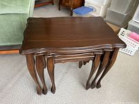 Side view of all three nesting tables stacked together, showing the curved legs and scalloped edges.