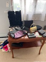 Photo showing black textured scarf hung on hanger and assortment of purses and wallets on wooden table.