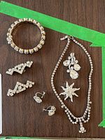 Full view of all jewelry items on wooden surface showing bracelet, necklace, earrings, and brooches
