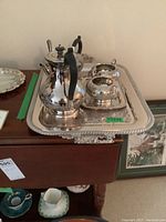 Silver plated tea and coffee pots with creamer and sugar bowl on ornate trays.