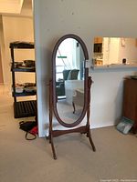 Front view of a wood framed free standing oval mirror with stand in a room.