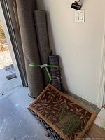 Rolled carpets and decorative doormat positioned upright and on floor in a garage