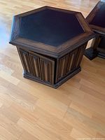 Hexagonal dark oak side table with black leather inlay top and detailed vertical carved wood panels on cabinet door and sides.