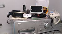 Various electronic devices featuring a Sony cassette player/radio, white landline phone, AT&T cordless phone, and a Spice modem sitting on top of an LG washing machine.