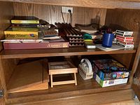 Multiple board games and card games including Scrabble and Play Nine, wooden trays, and decks of cards stacked on a wooden shelf.