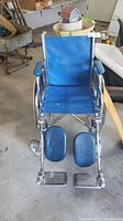 Front view of blue Invacare wheelchair showing seat, armrests, leg rests, and front wheels.