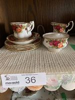 View of the stacked plates, tea cup on saucer, and sugar bowl displaying floral patterns and gold trim.