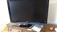 Front view of Sony Bravia 42 inch LCD TV on stand with remote and manual on shelf beneath.