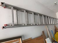 Full length of the steel extendable ladder against wall showing rungs and red end caps.