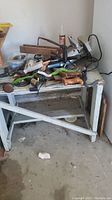 Overview of white wooden workbench with multiple tools including a corded skill saw, hand saws, and other hand tools scattered on top