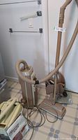 Vintage Electrolux cannister vacuum with hose, metal wand, and floor vacuum head on tiled floor in laundry room