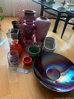 Overview of various vases including ceramic, glass, and pottery pieces in multiple colors and sizes, arranged on a wooden floor near furniture.