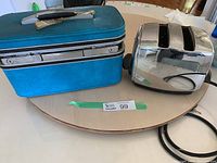 Photo showing teal blue Samsonite vintage train travel case with black handle, silver metal trim, locks, placed next to chrome Sunbeam two-slice toaster with attached cord.